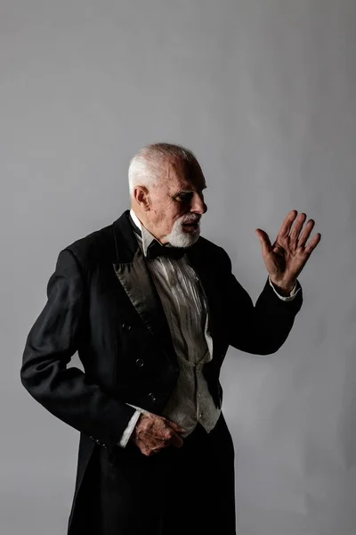 Old man in a tailcoat. Portrait of a bearded old man. Senior man dressed in a tailcoat on gray background.