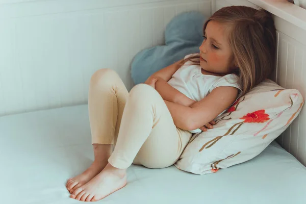 Lilla flickan i hennes säng har en magont. — Stockfoto