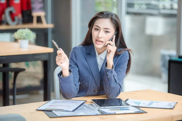 Young attractive woman making call to her bank service for consulting last transactions while is using online banking on laptop computer. Female business person having smartphone conversation