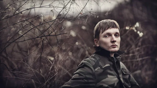 Attractive young man outdoors.Closeup portrait of a young handsome man .A sad young man in the forest. Photo in a dark style.