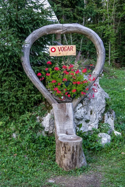 Close up view of wooden hiking sign (Vogar) with red flowers. Kosijev dom na Vogar Mountain Hut. Summer in Triglav National Park, Slovenia.