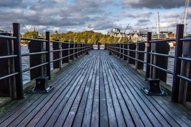 Landscape view of wooden platform on the river Thames.Trees and buildings in the background. London, United Kingdom. clipart