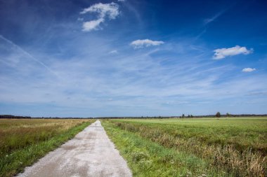 Ufuk ve beyaz bulutların üstünde mavi bir gökyüzü doğru uzun çakıl yol