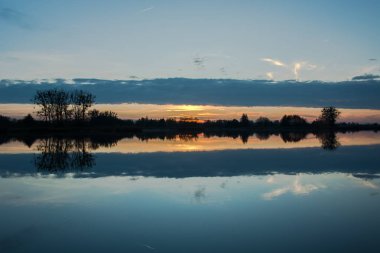 Günbatımı ve ağaçlar sahilde sırasında göle yansıtan bir kara bulut