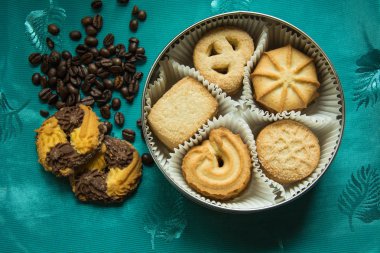 Yuvarlak bir kutu ve üzerinde yeşil bir masa örtüsü kahve çekirdekleri ile yalan iki şekerli kurabiye