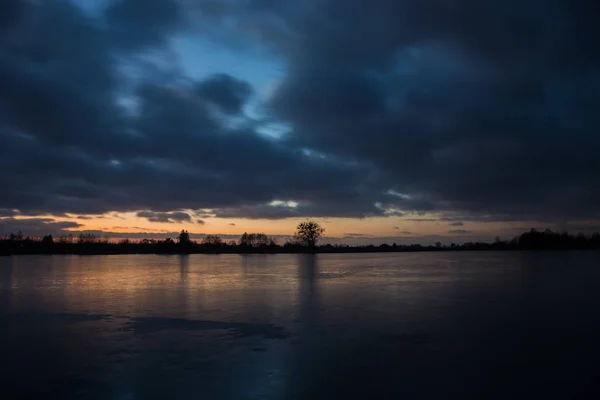 Bewolkte Donkere Hemel Zonsondergang Een Bevroren Meer Reflecterende Licht Het — Stockfoto