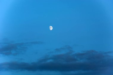Moon on a blue sky over dark clouds