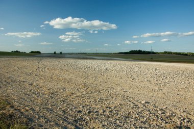 Sürülmüş alan, ufuk ve beyaz bulutların üzerinde mavi bir gökyüzü