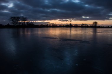 Donmuş bir gölün üzerinde gün batımı ve yansıtan sonra bulutlu karanlık bulutlar 
