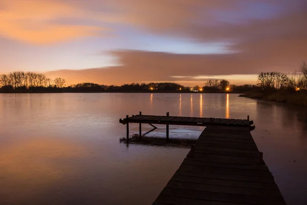 Houten brug met planken op een bevroren meer en wolken na zonnen — Stockfoto