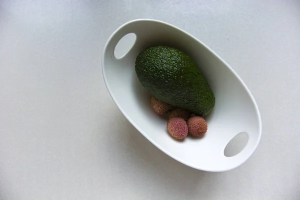Green avocado and litchi fruits in a white bowl
