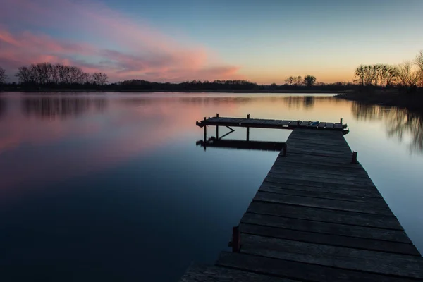 Brug op een kalm meer en roze wolken na zonsondergang — Stockfoto