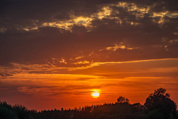 The setting sun behind trees and dark clouds. Nowiny, Poland