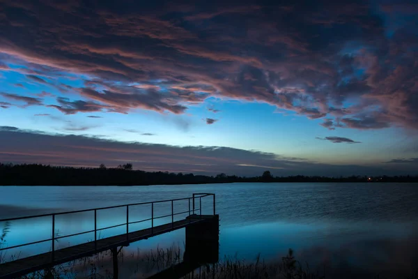 Nuages éclairés au-dessus du lac avec une jetée — Photo