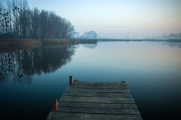 Jetty feito de tábuas, árvores e um lago nebuloso — Fotografia de Stock