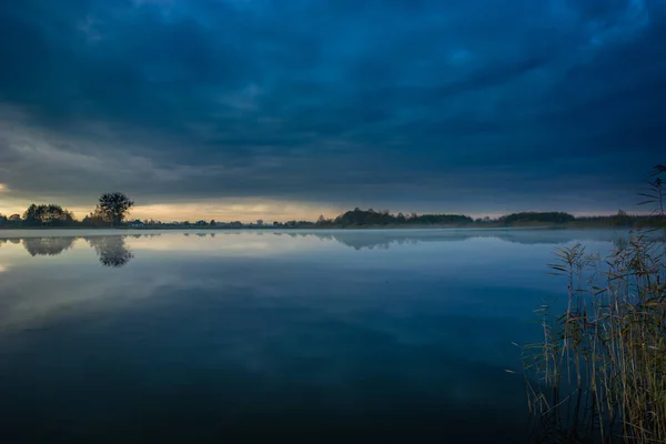 Donker blauwe wolken boven het meer met mist en riet — Stockfoto