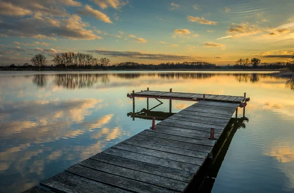 Pier op het meer, reflectie van wolken in het water na zonsondergang — Stockfoto