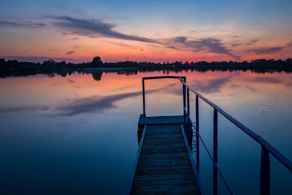 Jetty con una barandilla en el lago, horizonte y noche nubes de colores en el cielo — Foto de Stock