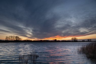 Güneş battıktan sonra sazlıklarla dolu sakin bir gölün üzerinde fantastik bulutlar.