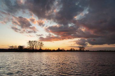 Gün batımından sonra karanlık bulutlar huzurlu bir gölde, akşam yürüyüşü manzarası