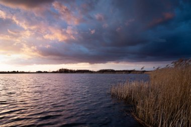 Gün batımından sonra gölde sazlıklarla kara bulutlar.