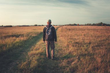 Vahşi doğada, toprak yolda ve gökyüzünde küçük bir sırt çantası olan bir gezgin.