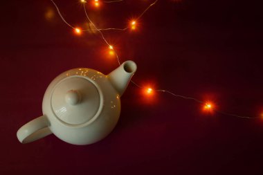 Beyaz seramik çaydanlık ve kırmızı arka planda Noel ışıkları, üst manzara.
