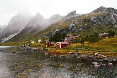Norveç'te Lofoten Adaları arka planda dağlar ile Vinstad kıyısında uzak bir eski balıkçı köyüpanoramik görünümü.
