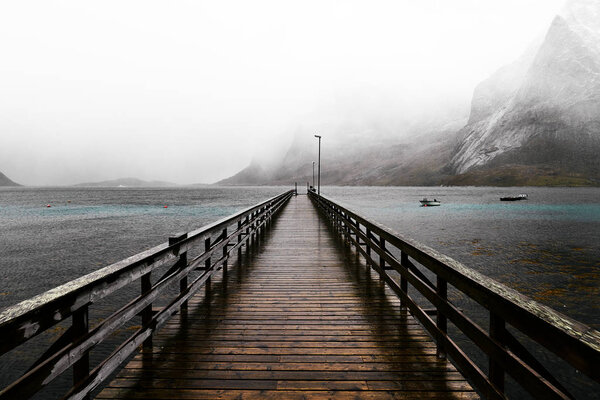 Wooden bridge on the arctic ocean in Vinstad leading into the distance on a cold day in the winter. In the background one can see the snowcapped mountains.