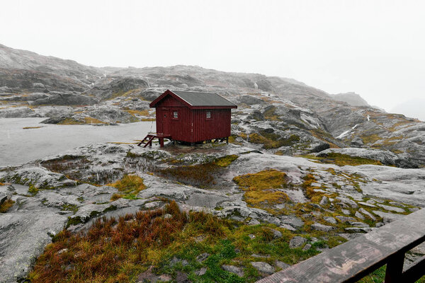 Дистанционная изолированная красная деревянная хижина в скалистых горах на Лофотене в Норвегии рядом с озером во время сильного шторма и дождя
.