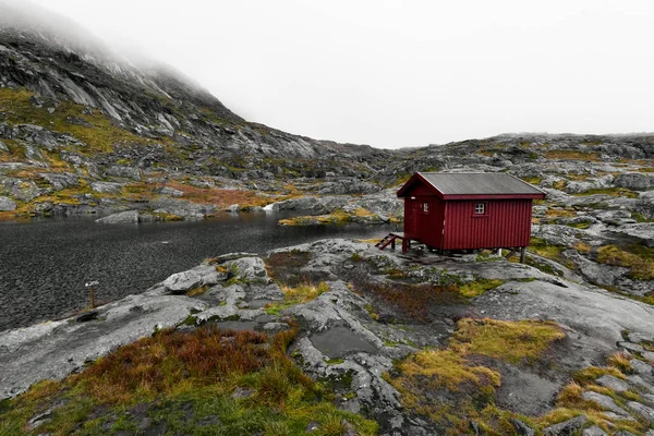 Remote isolated red wooden cabin in the rocky mountains on Lofoten in Norway next to a lake during a heavy storm and rain.
