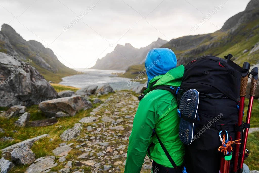 Young man with a backpacking hiking to a beautiful bay surrounded by mountains on Lofoten Islands in Norway 