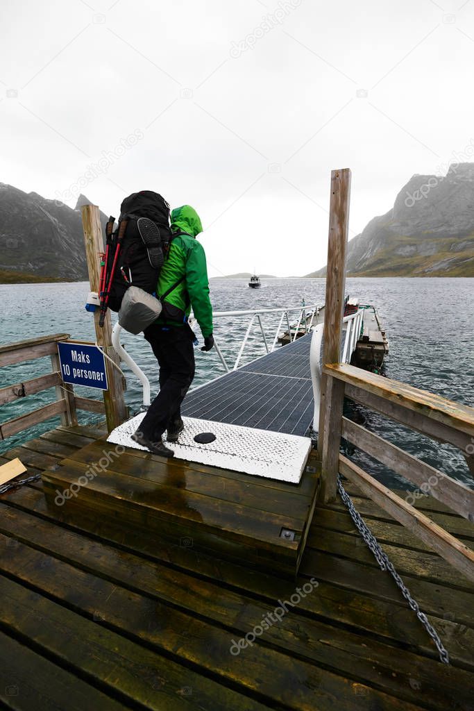 Man with a backpack waiting at a jetty for the arriving ferry boat to drive from Vinstad to Reine on Lofoten in Norway