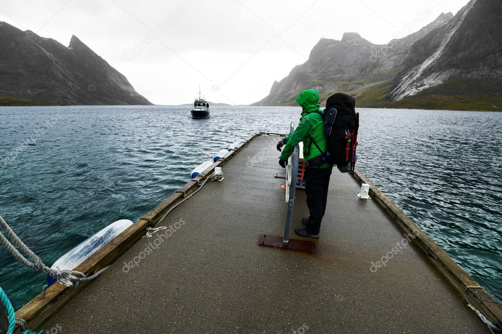 Man with a backpack waiting at a jetty for the arriving ferry boat to drive from Vinstad to Reine on Lofoten in Norway