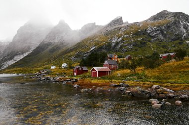 Norveç'te Lofoten Adaları arka planda dağlar ile Vinstad kıyısında uzak bir eski balıkçı köyüpanoramik görünümü.