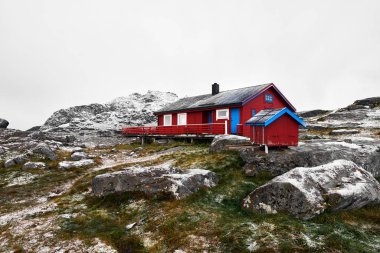 Norveç'te Lofoten Adaları'nda karla kaplı dağların tepesinde kırmızı ahşap fredvang kabin.