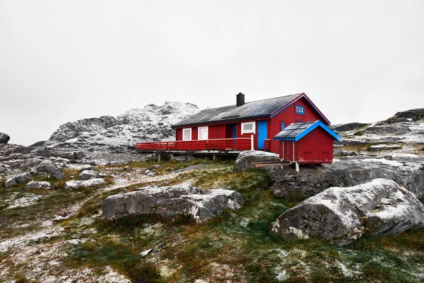 Norveç'te Lofoten Adaları'nda karla kaplı dağların tepesinde kırmızı ahşap fredvang kabin.