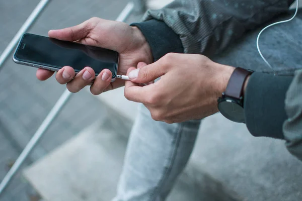 No life without music. Close-up part of young man adjusting his headphones while holding his smartphone