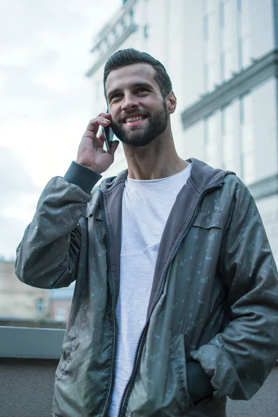 See you later! Handsome young man using his smartphone and looking away with smile while standing outdoors