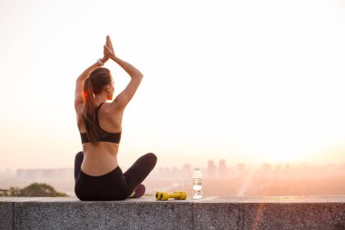 Namaste yeni güne diyerek. Spor giyim sanayi kenti görünümü karşı otururken yoga yaparken arka uygun görünümünü genç güzel kadın