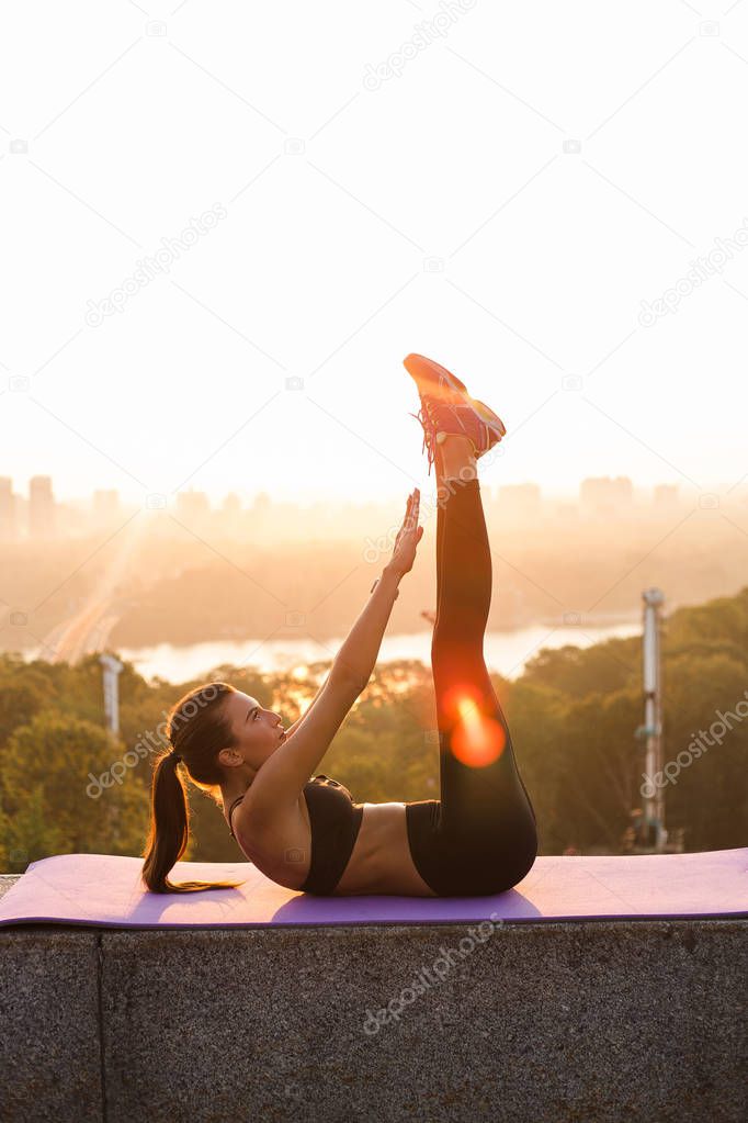 Feel the burn in muscles. Full length of young beautiful fit woman in sportswear exercising and putting her legs up while lying down against industrial city view