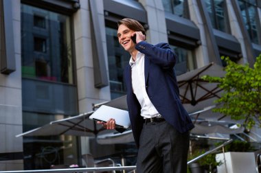 Yeni office bulduk! Onun laptop taşıyan ve açık havada duran süre gülümseme ile onun smartphone kullanarak yakışıklı delikanlı