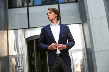 Modern iş adamı. Ceketini ayarlama ve uzak açık havada duran süre seyir yakışıklı genç adam