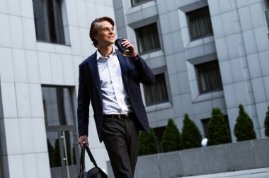 Harika bir gün. Yakışıklı genç adam onun çanta taşıyor ve kahve fincanı açık havada süre ayakta tutan