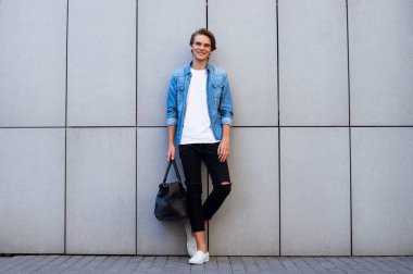 Yeni gün için hazır. Yakışıklı genç adam kameraya gülümseme ile seyir ve açık havada duran ise büyük çanta taşıyor tam uzunlukta