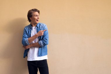 Buraya bak! Uzak duran sarı arka plana karşı gülümseme ile işaret eden yakışıklı genç