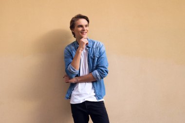 Tatlı mavi gömlekli. Uzak gülümseme ile seyir ve çene duran sarı arka plana karşı el tutmak yakışıklı genç adam