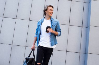 Neşeli ve şık. Kahve fincanı tutarak ve uzak açık havada yürürken gülümseme ile seyir yakışıklı genç adam