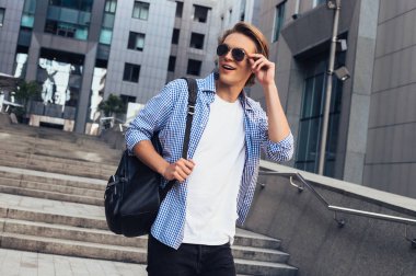 Awesome arıyor. Yakışıklı genç adam uzakta açık havada yürürken gülümseme ile seyir güneş gözlüğü 