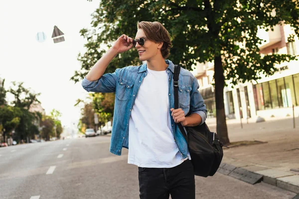 Bu sabah için mükemmel stil. Güneş gözlüklerini ayarlama ve uzak açık havada gülümseme ile yürürken seyir yakışıklı genç adam